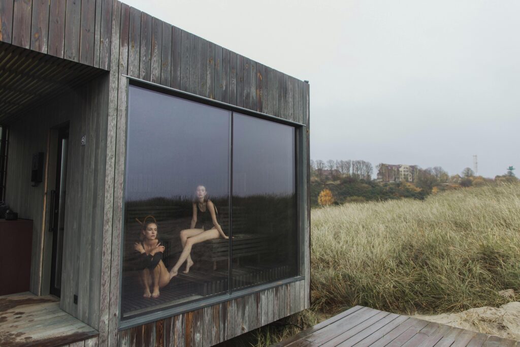 pexels-photo-5979571-5979571 Two women in swimsuits relaxing in a wooden sauna with glass window overlooking nature.