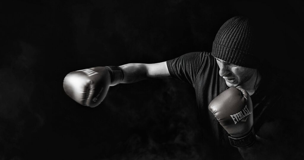 Monsieur habillé en noir avec des gants de box et un bonnet. Il est en train de faire un mouvement 