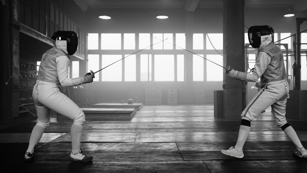 Two fencers engaging in a fierce duel inside a well-lit gym.
