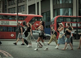 Crowd crossing a London street with iconic red buses in motion, capturing urban life.